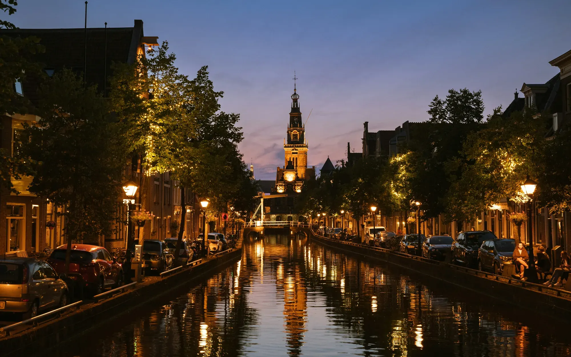 The lit Waagtoren tower at the end of an Alkmaar canal at dusk