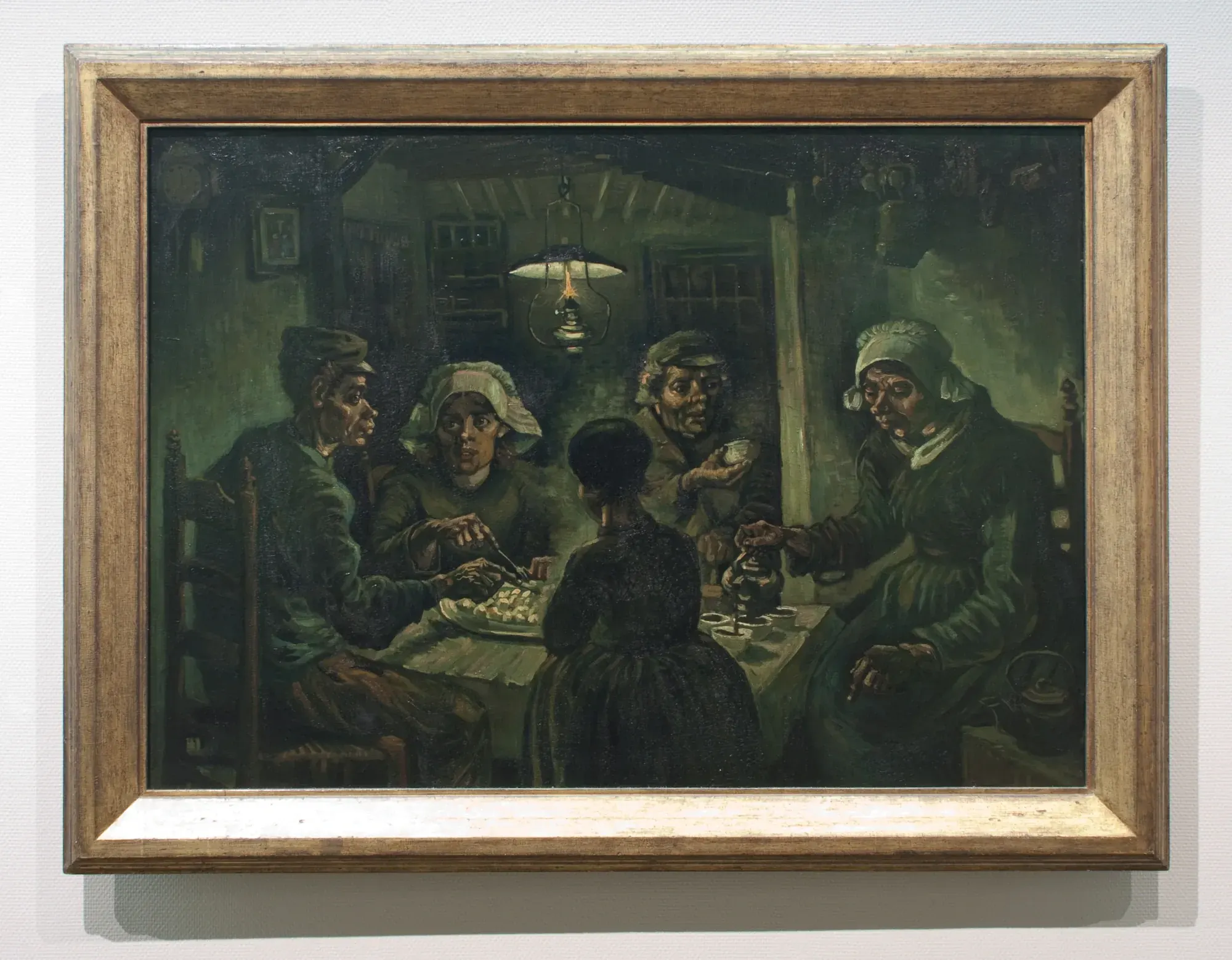 Van Gogh's The Potato Eaters (1885) in its gold frame on the gallery wall of the Van Gogh Museum, Amsterdam