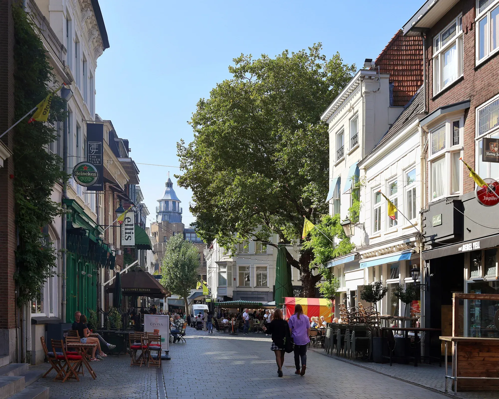 The Sint Janstraat in Breda with cafe terraces and the Grote Kerk tower at the end of the street