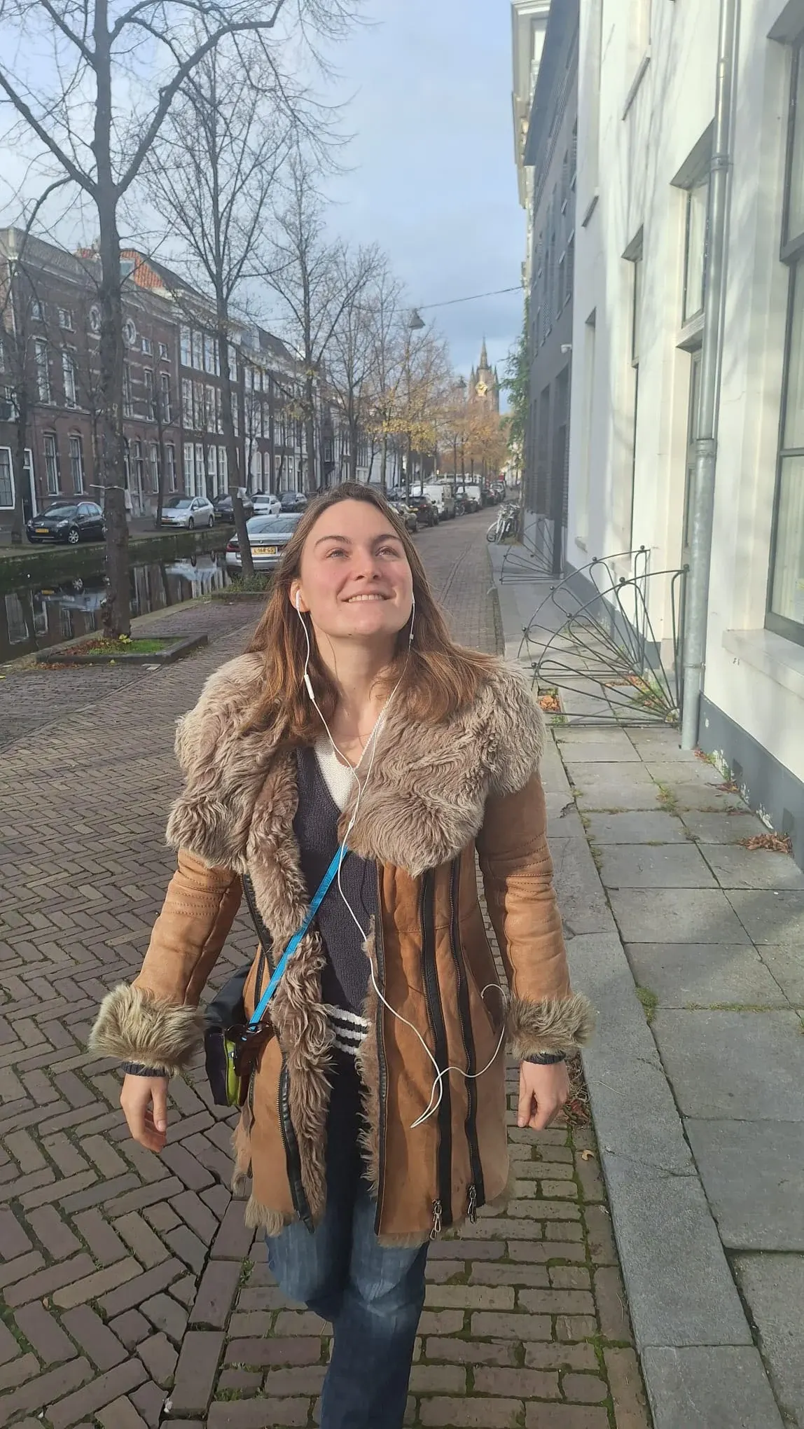 A woman walking beside a Delft canal with earphones in, listening to the audio tour