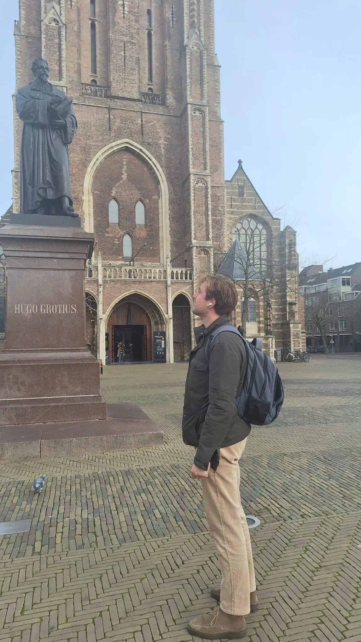 A listener with earphones in looking up at the statue of Hugo Grotius on the Markt in Delft