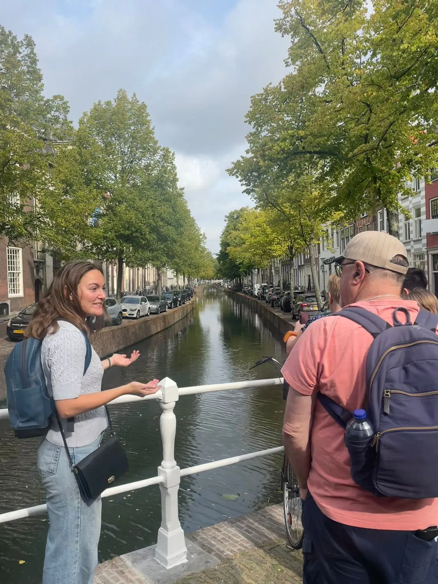 A guide explaining local history to a guest on a Delft canal bridge