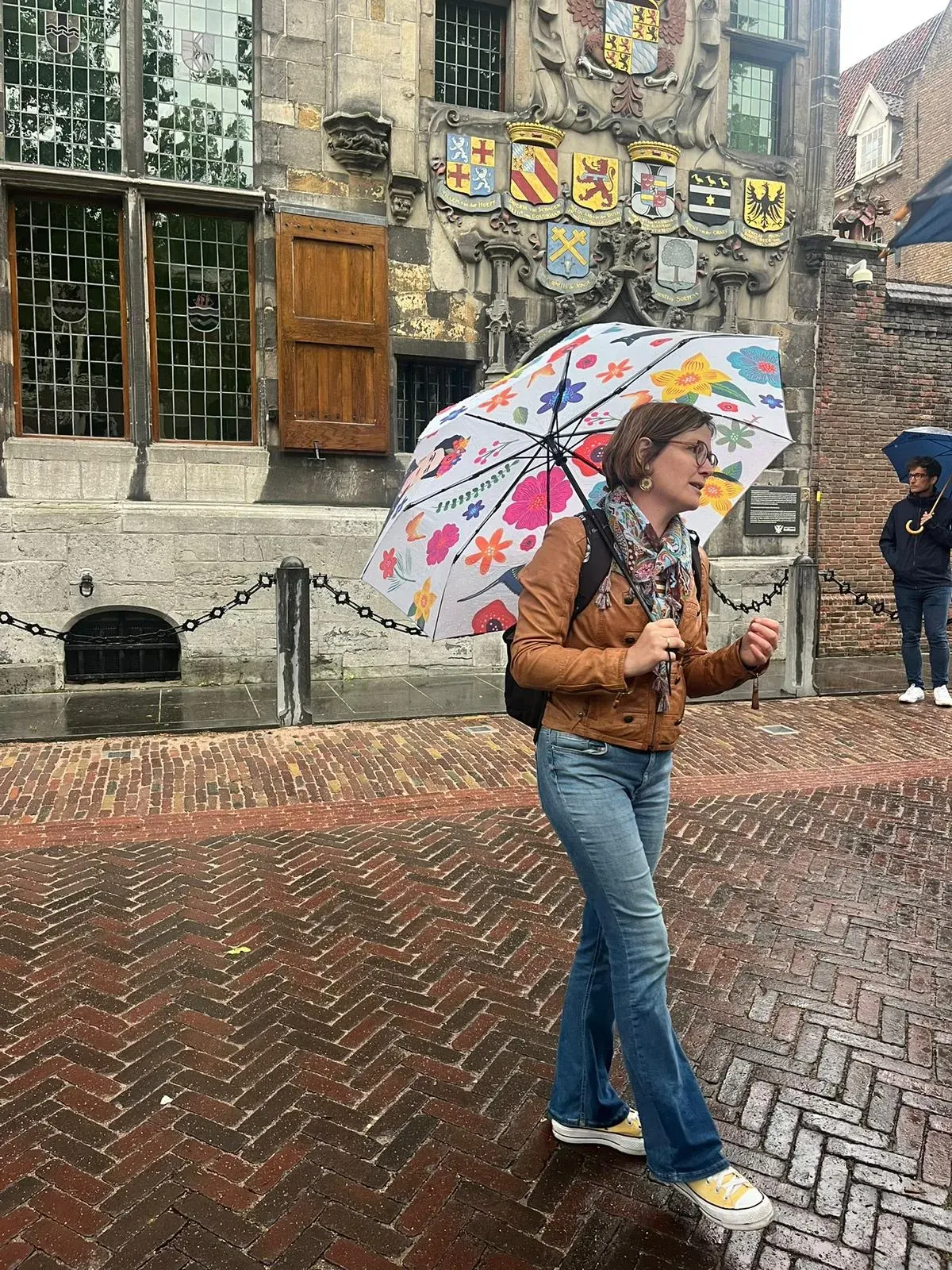 A guide with an umbrella passing the Gemeenlandshuis facade decorated with heraldic shields, Delft