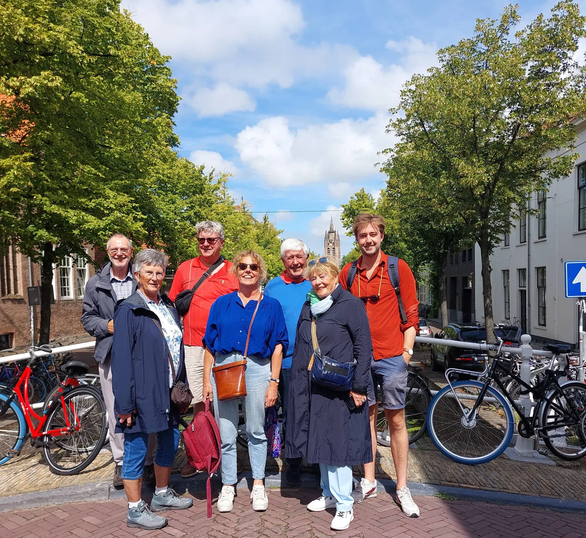 A guide and a small tour group on a canal bridge in Delft, with the leaning tower of the Oude Kerk behind them