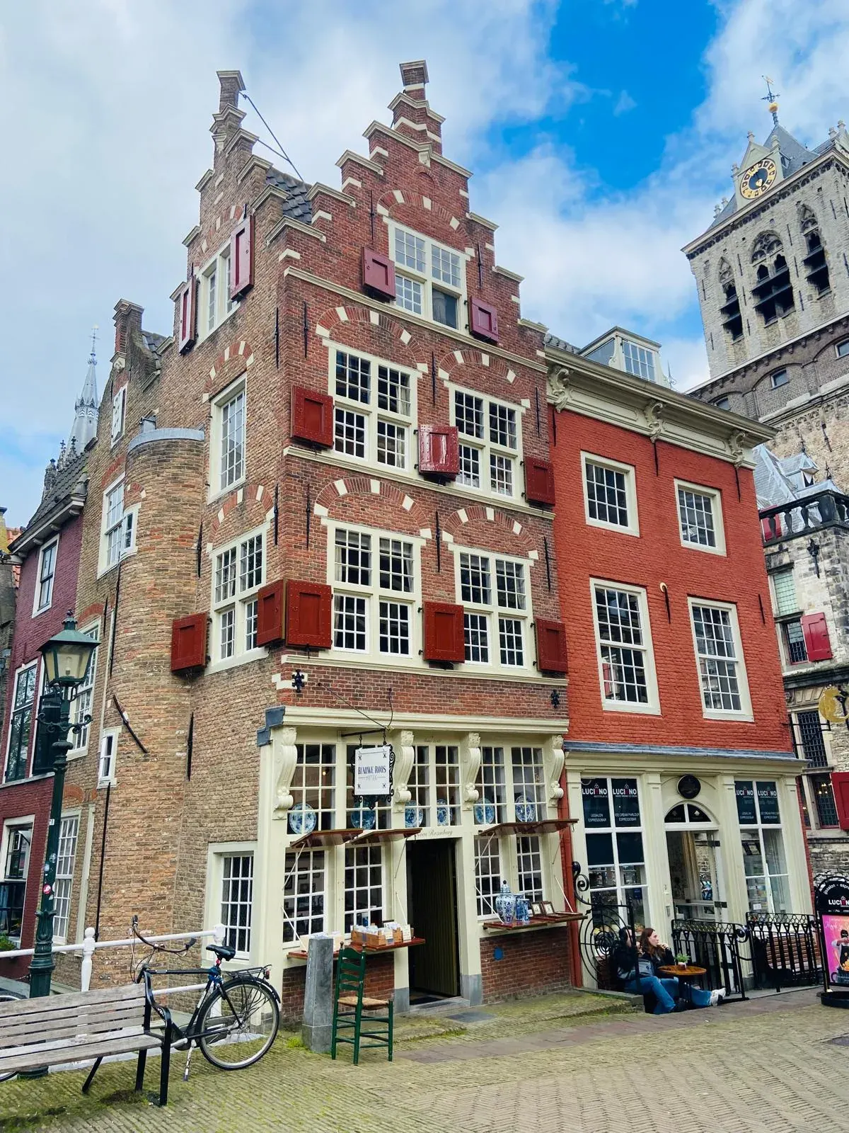 A corner house with a Delftware shop sign and the Nieuwe Kerk tower behind, Delft
