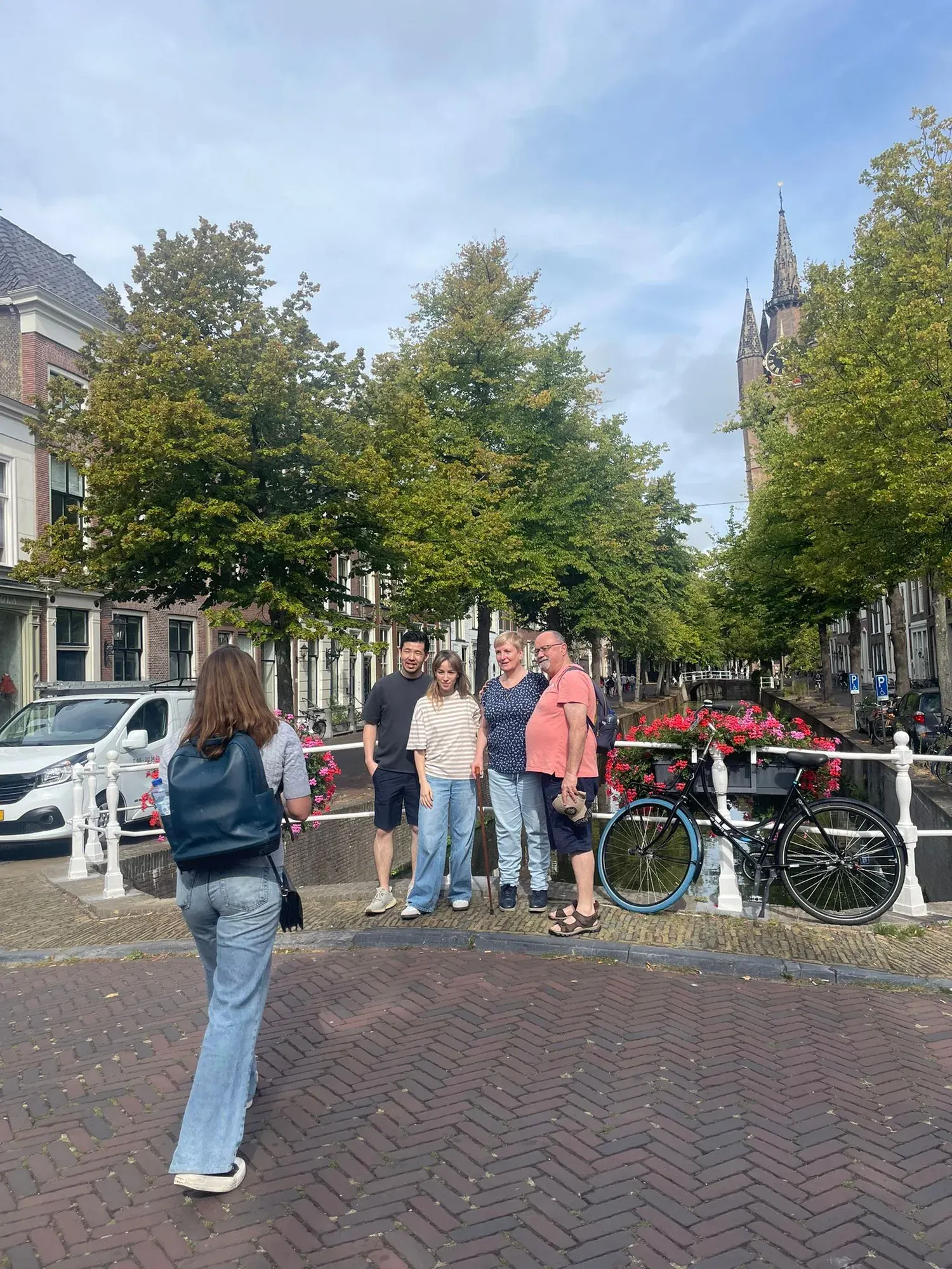 A small private tour group posing on a canal bridge with a church tower behind, Delft
