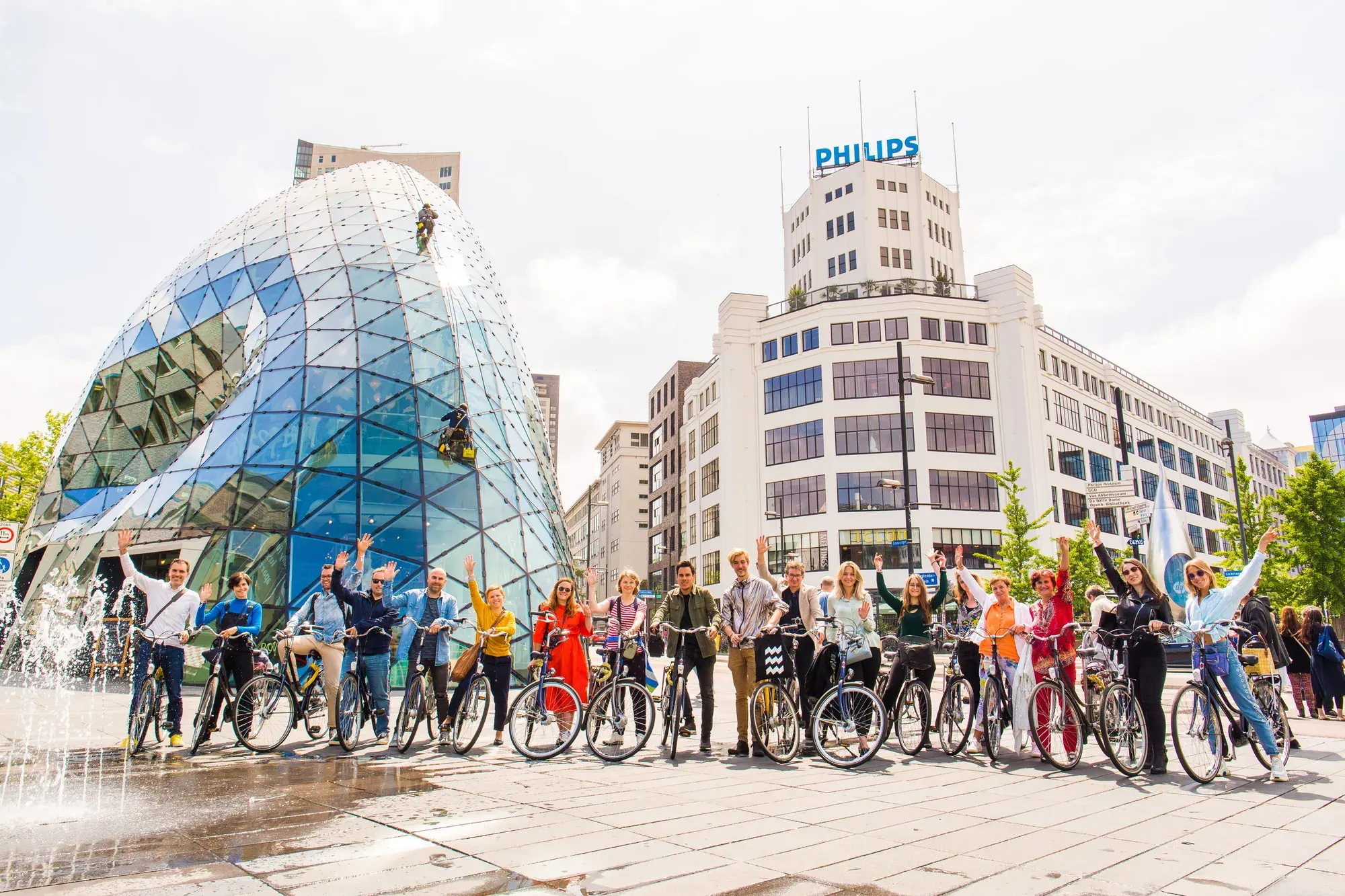 A line of cyclists in front of the glass Blob and the Philips Lichttoren, Eindhoven