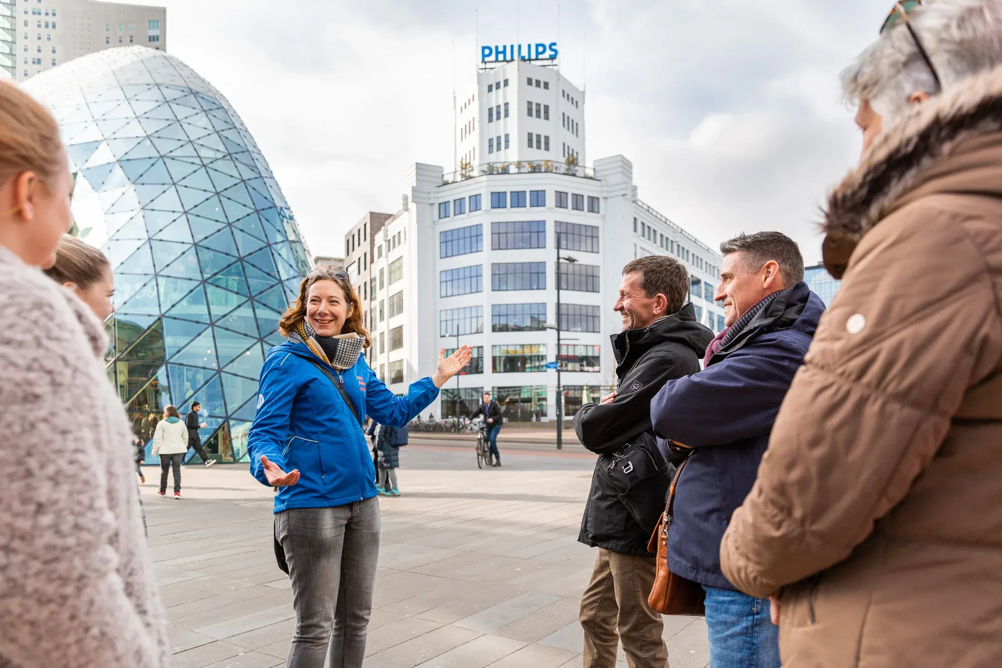 A guide talking to a small group on 18 Septemberplein in Eindhoven, with the Blob and the Philips Lichttoren behind