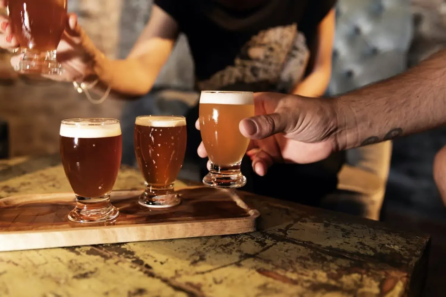 A tasting flight of three Dutch beers on a wooden paddle, one glass being lifted