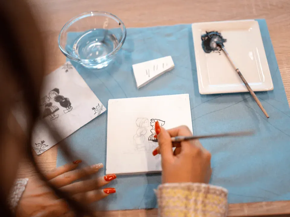 Hands painting a blue design onto a white tile at a Delftware workshop
