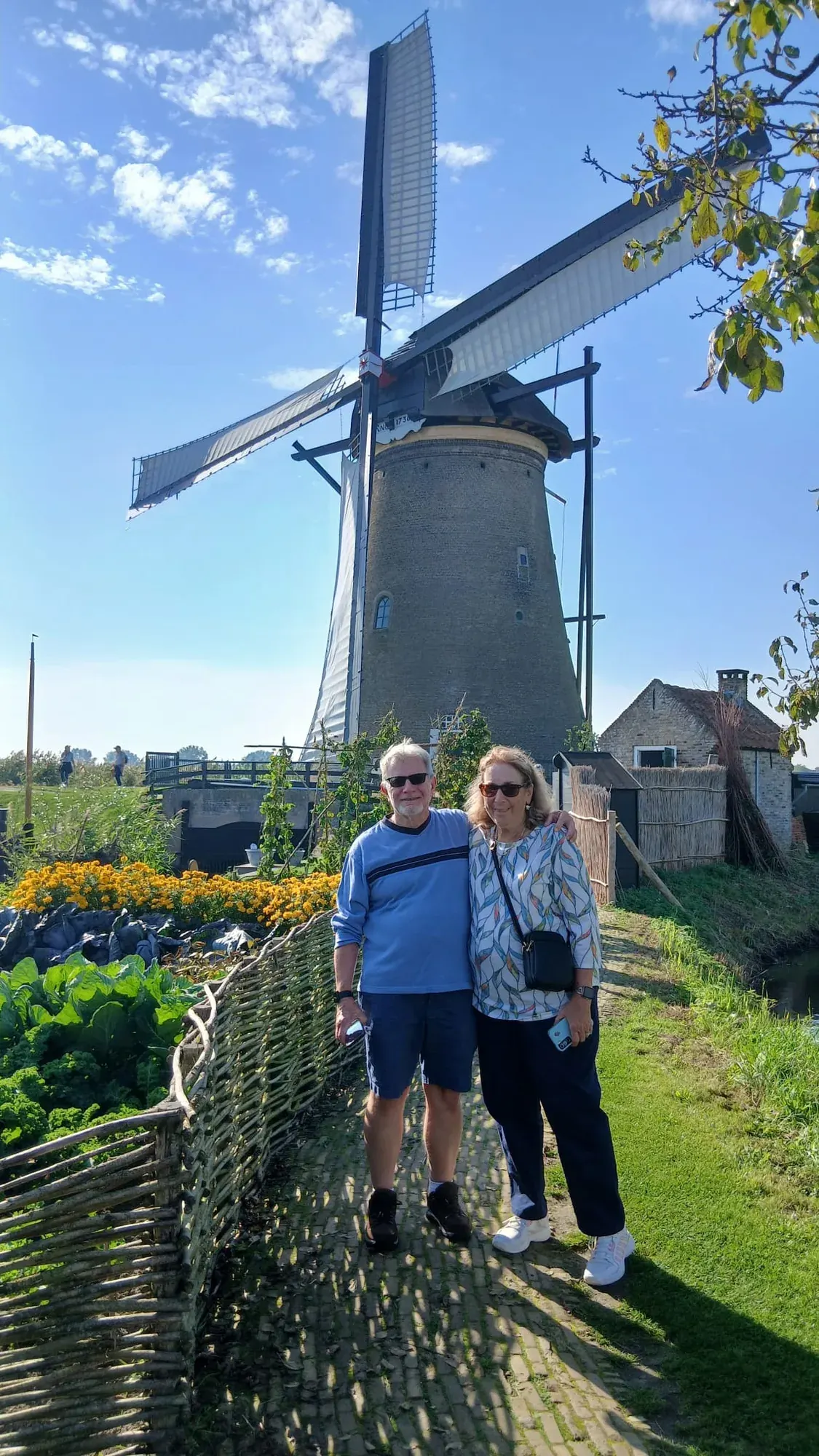 Two visitors in front of a windmill and its vegetable garden at Kinderdijk