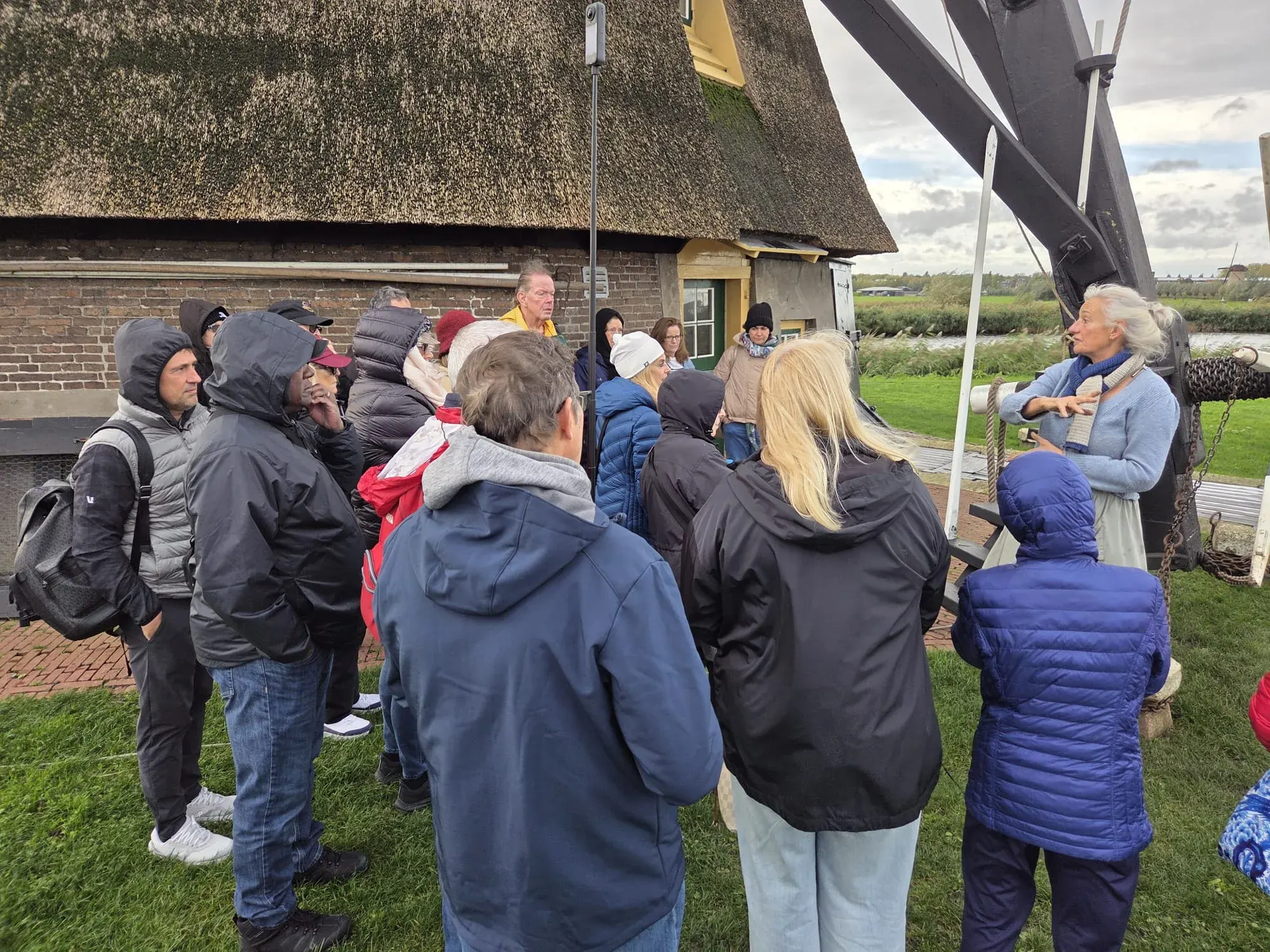 Eine Gruppe hört dem Guide neben einer reetgedeckten Windmühle zu