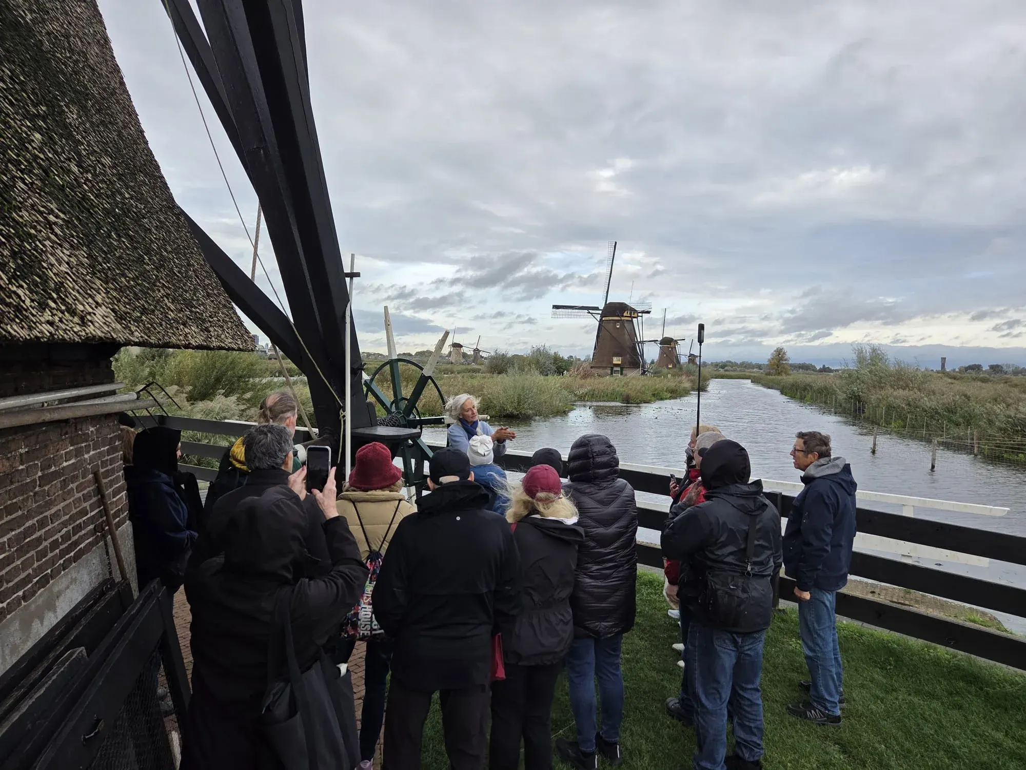 Eine kleine Gruppe mit einem Müller neben einer Windmühle in Kinderdijk, dahinter weitere Mühlen am Kanal