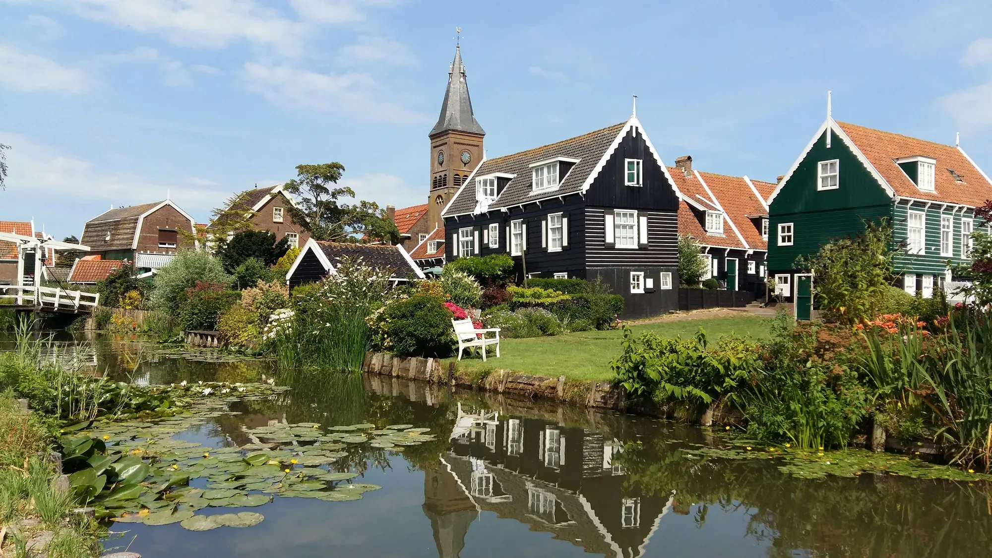 Timber houses and the church tower reflected in a pond in Marken