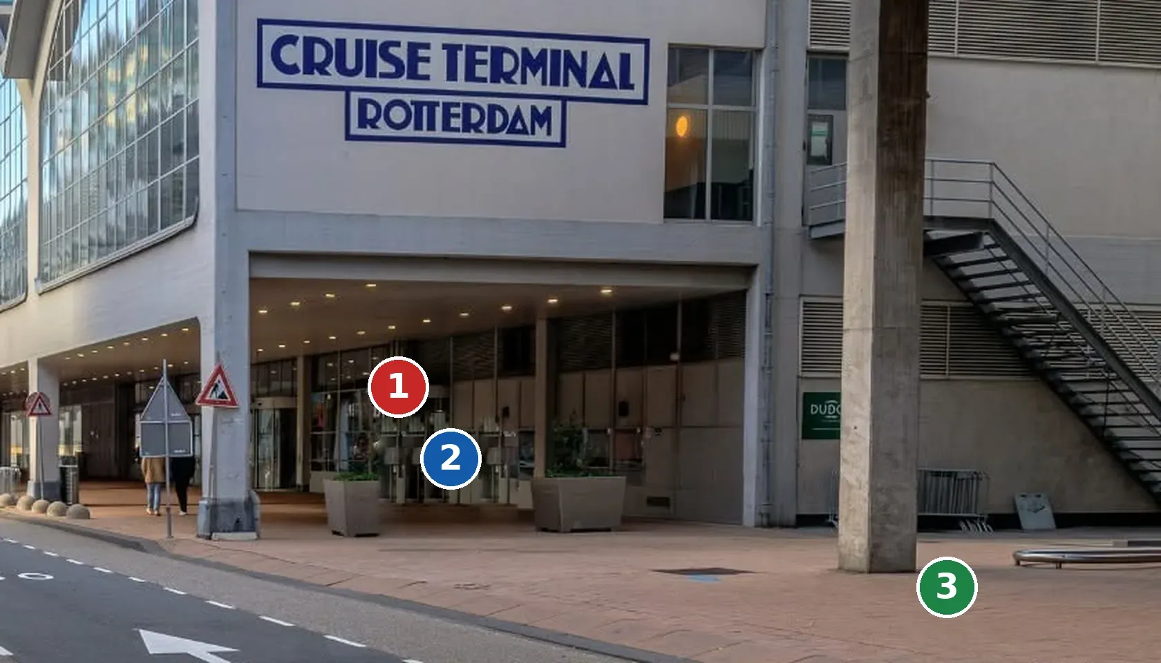 The exit of Cruise Terminal Rotterdam with three numbered markers: the exit door, the spot under the roof where the guide waits with a white sign, and the pavement by the concrete pillar where the minibus waits