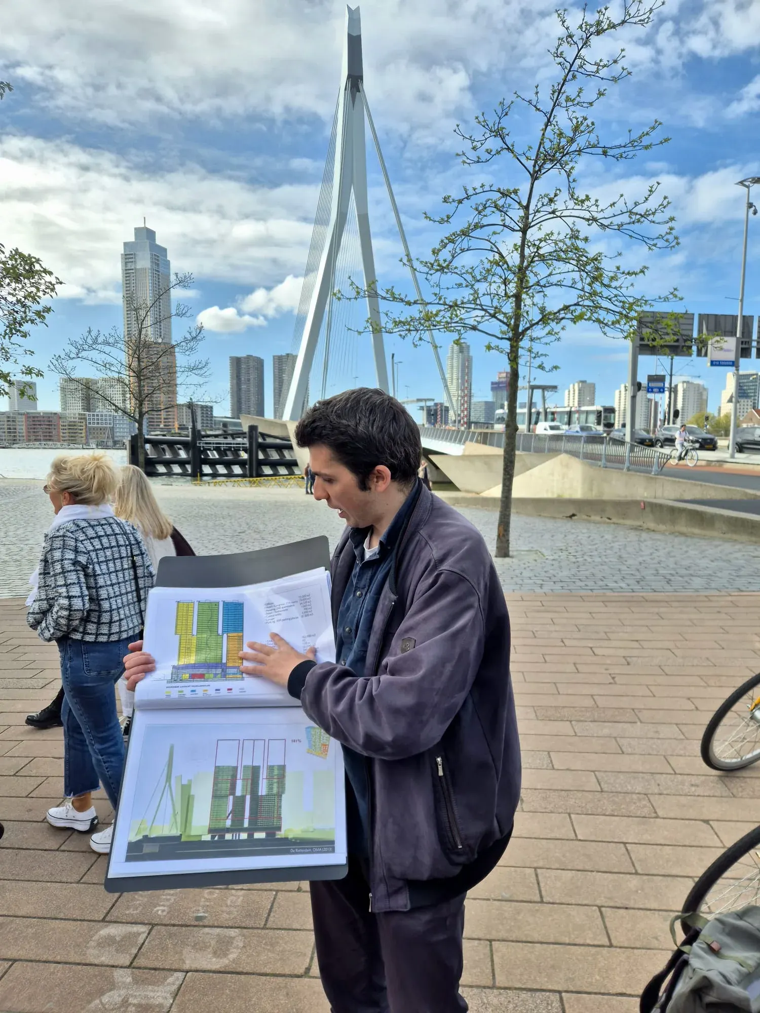 A Holland City Tours guide telling a story to guests with the Erasmusbrug behind them in Rotterdam