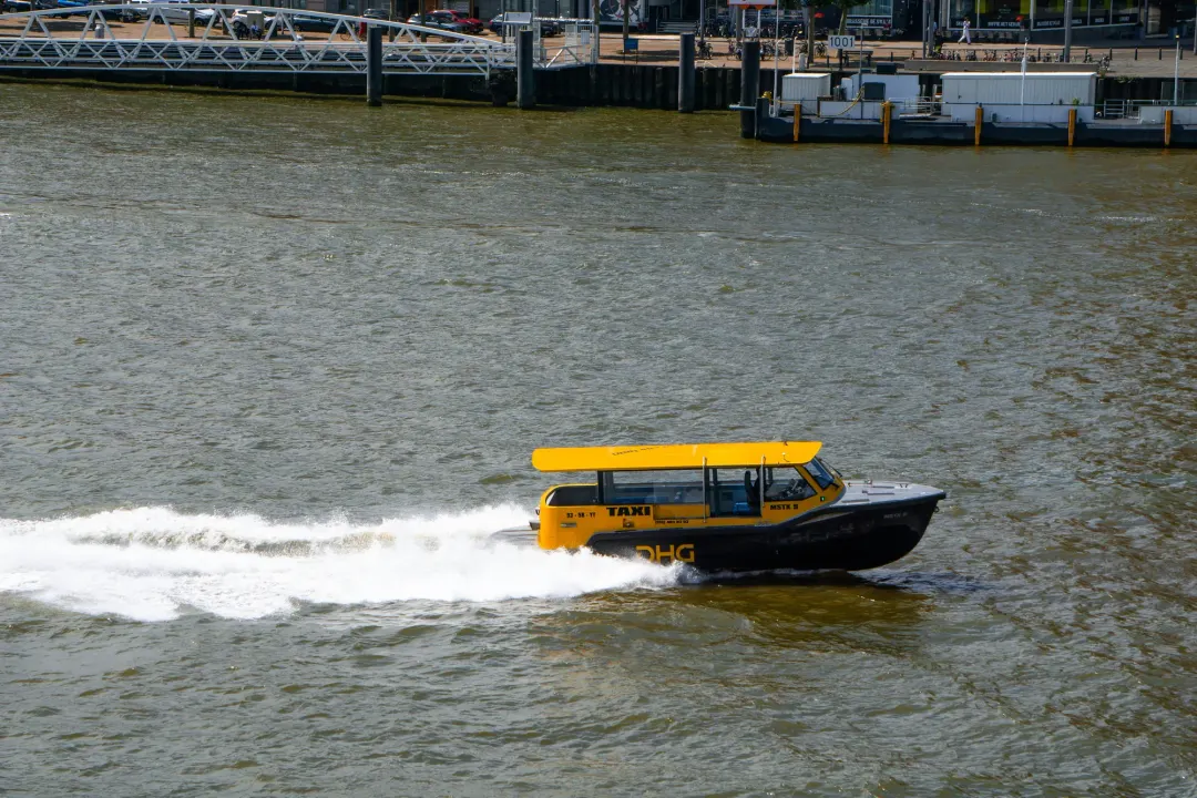 A yellow Rotterdam water taxi crossing the Nieuwe Maas at speed