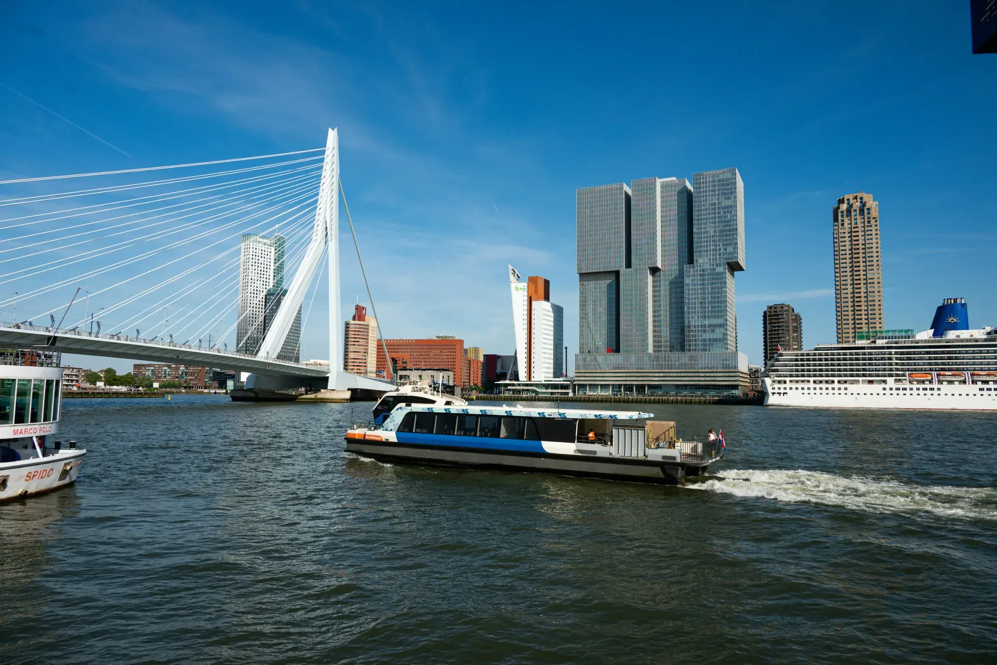 The WaterShuttle passing the Erasmusbrug in Rotterdam, with De Rotterdam and the Kop van Zuid skyline behind it