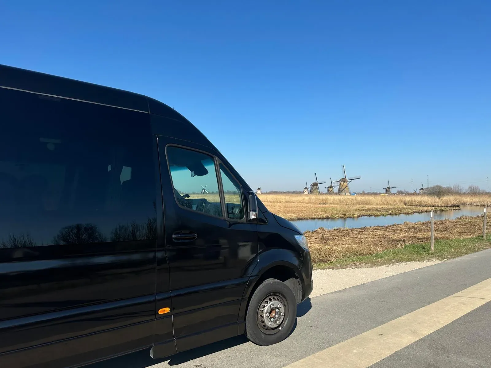 Der Minivan von Holland City Tours steht an einem Polderkanal bei Kinderdijk, dahinter die Windmühlen in einer Reihe über dem Feld