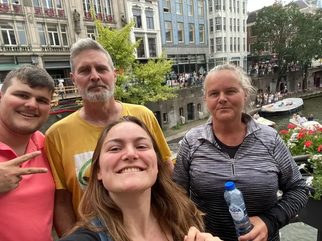 A guide and three smiling guests on the Oudegracht canal in Utrecht, boats and geraniums behind